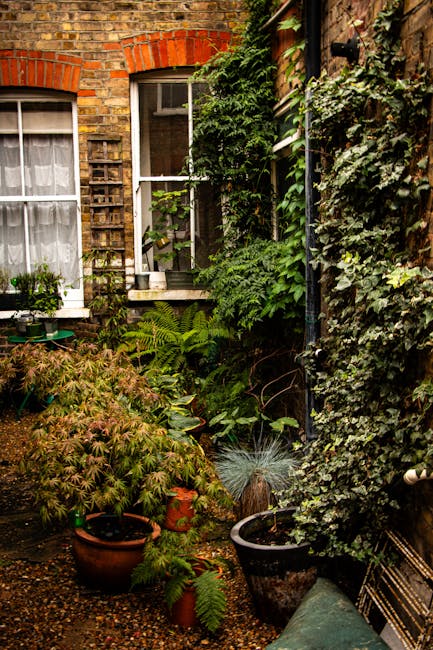 A collection of potted succulents and cacti on a small terrace balcony with a metal railing in the foreground. The pots contain various types of cacti, including round, spiny ones and elongated, flesh